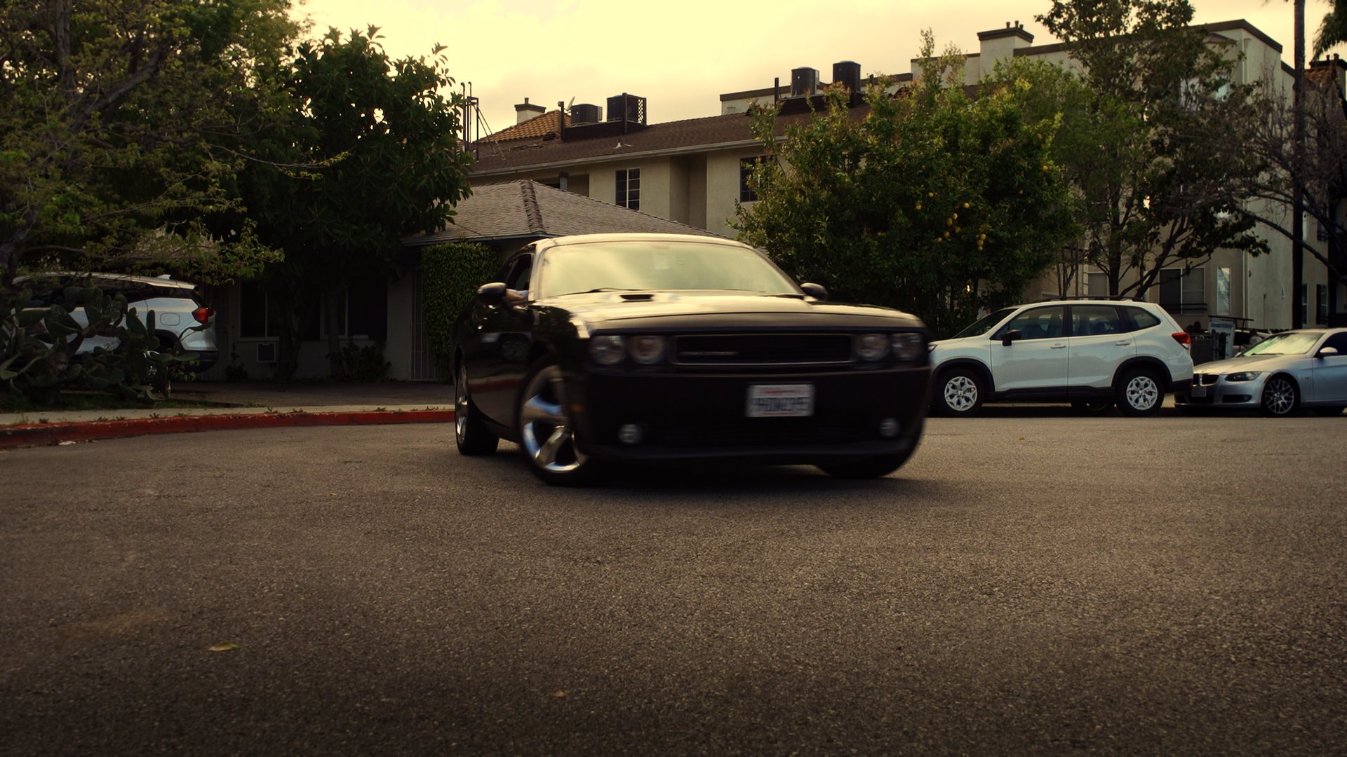 Still from God's Second Best Man: a black muscle car parked in a courtyard lot
