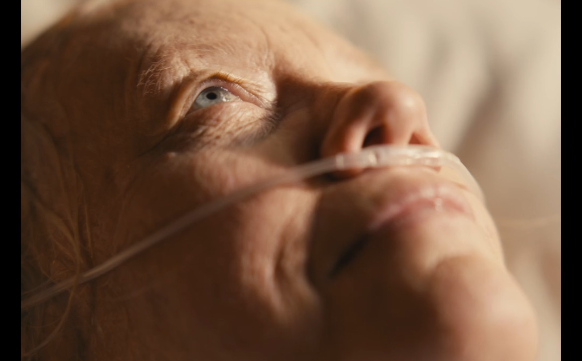 Still from What's Life: an elderly woman looking upward in soft light