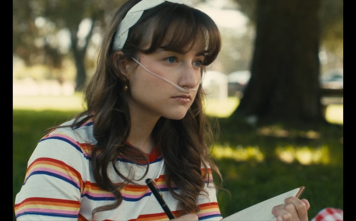 Still from What's Life: a girl in a striped shirt writing under a tree
