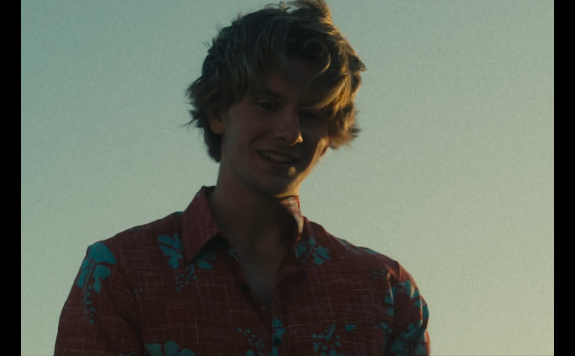 Still from What's Life: a boy in a floral shirt under an open sky